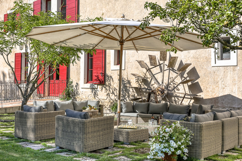 Shaded outdoor seating against the stone facade and its red shutters