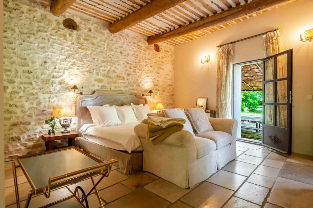 A bedroom with exposed stone wall and doors onto the garden